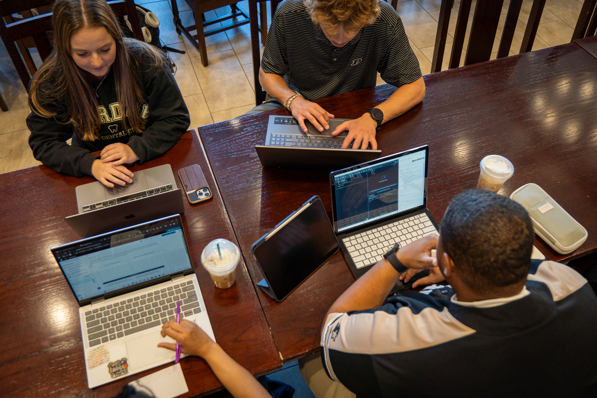 a top-down shot of 4 students sitting together looking at their individual laptops